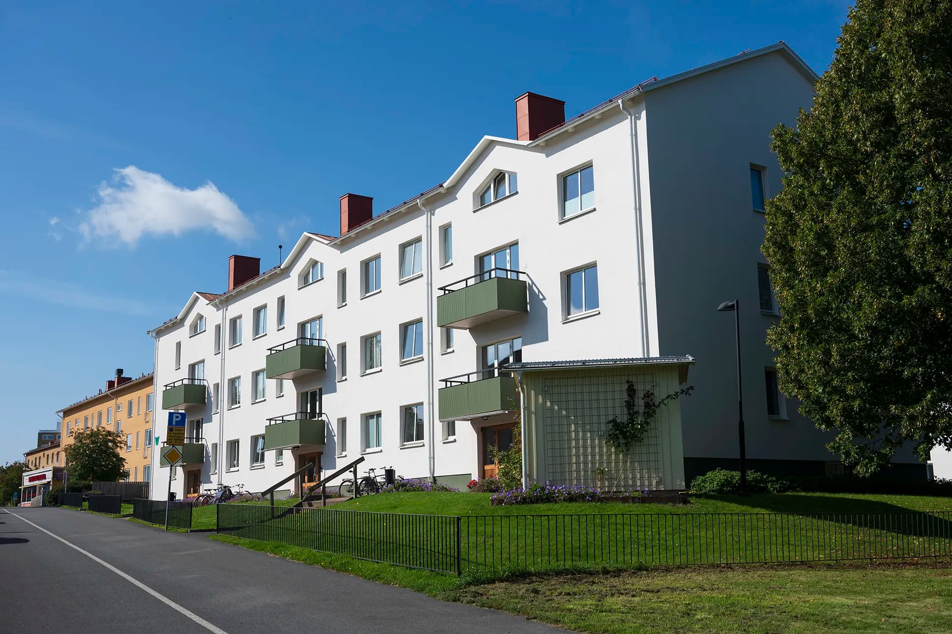 Flerfamiljshus med vit fasad och gröna balkonger och en grönskande gräsmatta