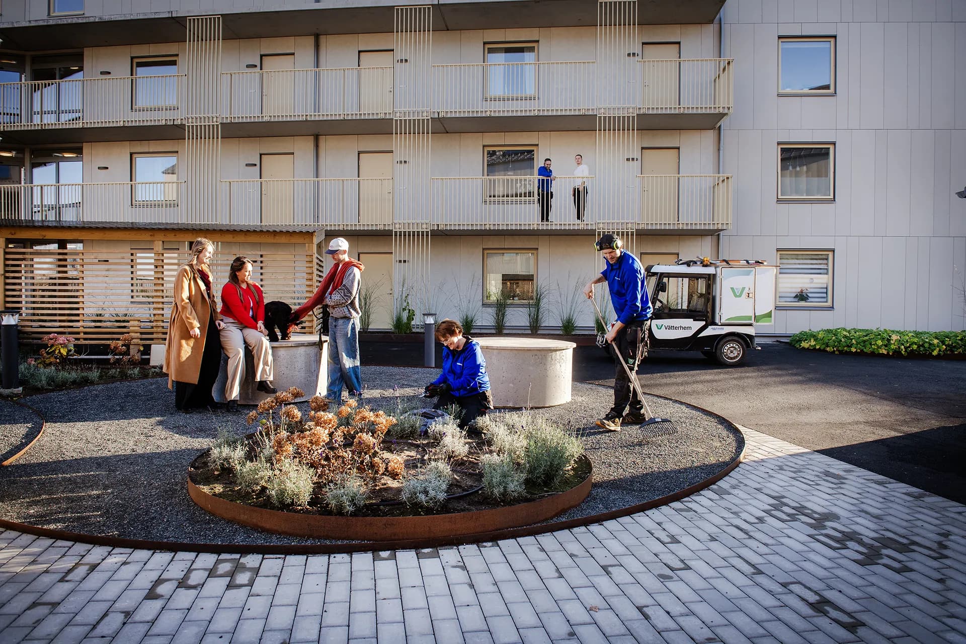Hyresgäster och arbetande parkvärdar på innergården framför ett hyreshus