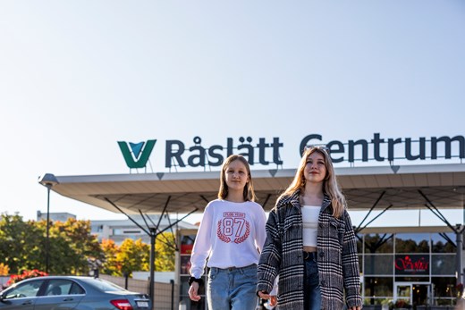 Två unga tjejer som går med Råslätt centrum i bakgrunden