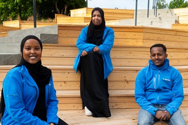 Tre personer som sitter i en trätrappa klädda i Vätterhems blå jackor