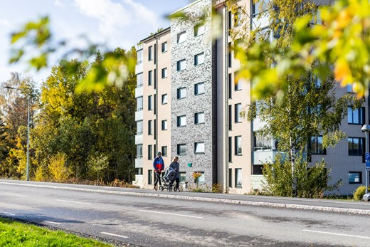 Par med barnvagn promenerar förbi lägenhetshus med höstfärgade träd runtom